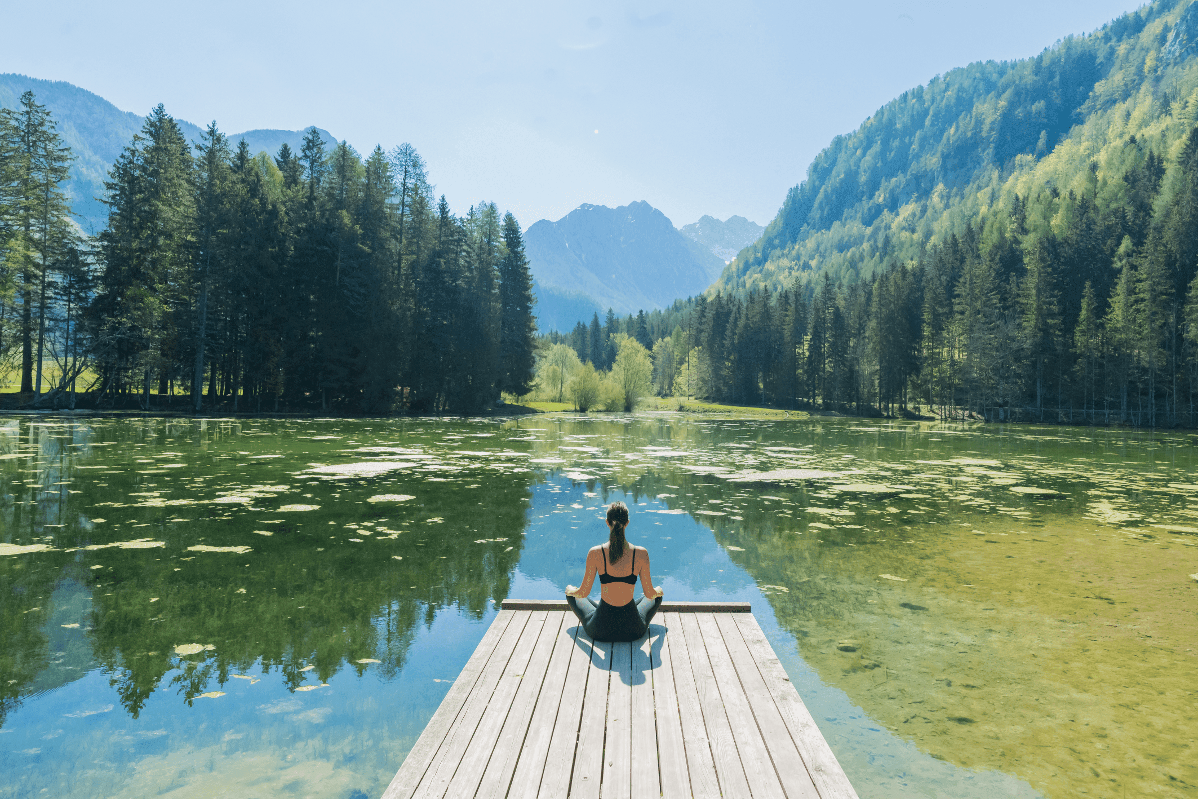 Person meditating on a dock overlooking a mountain lake